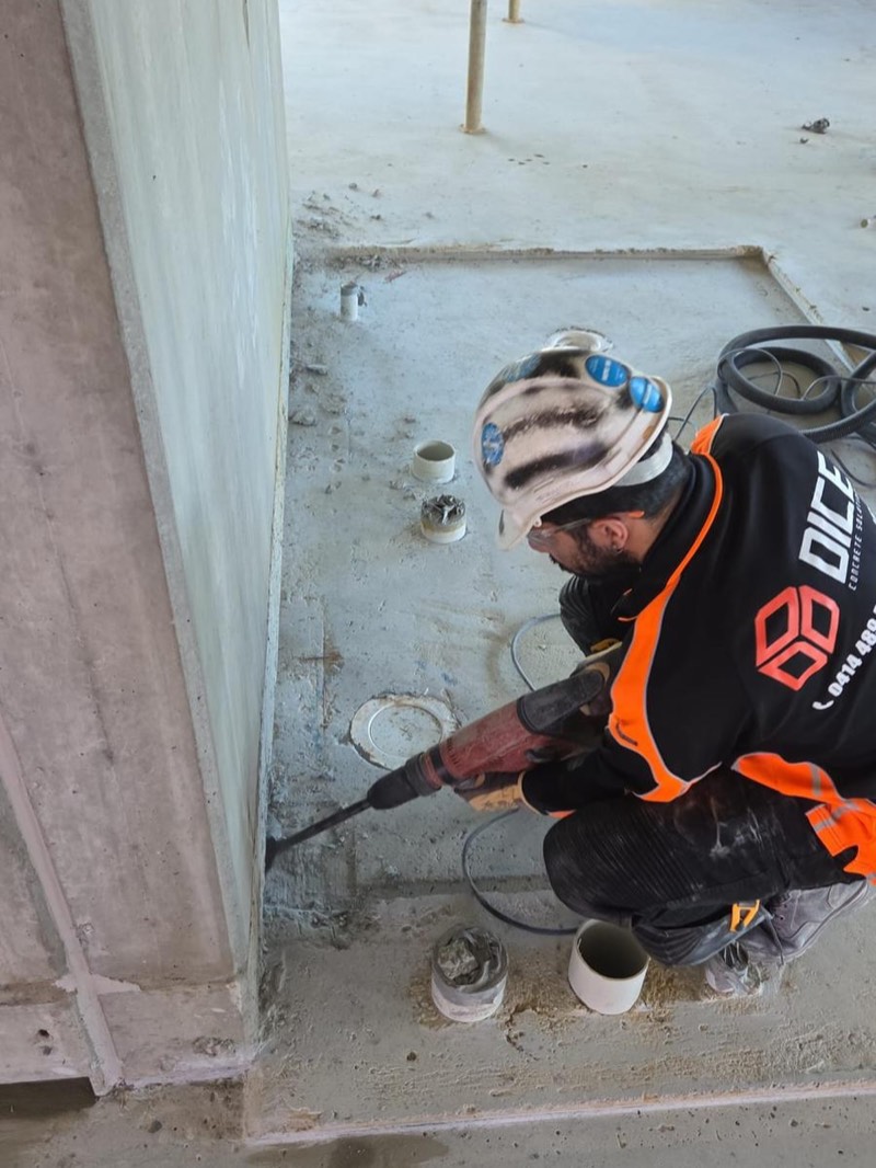 Worker using a rotary hammer around floor penetrations in a concrete slab.