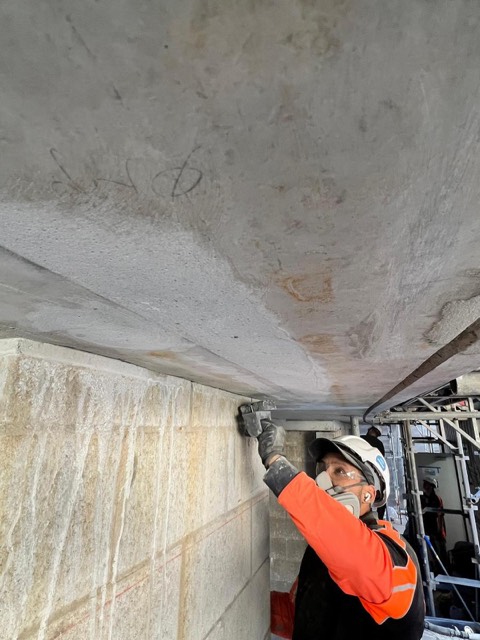 Dice Concrete Solutions tradesperson hand-trowelling a patch repair to a concrete soffit while wearing a respirator.