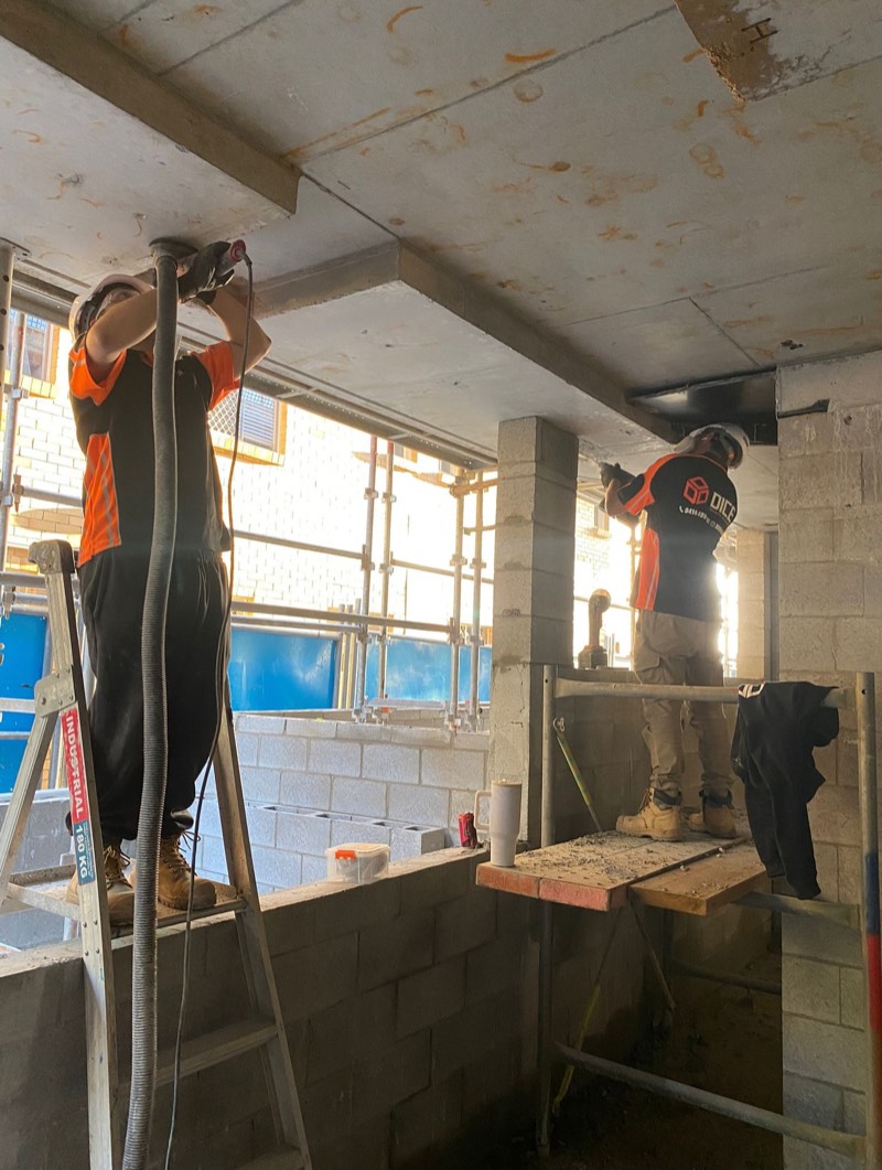 Two Dice Concrete Solutions workers grinding and preparing a concrete soffit from work platforms on a commercial site.